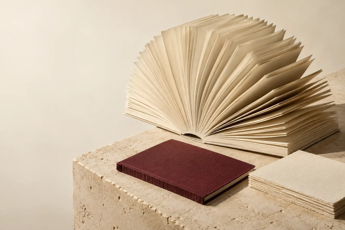 Sculptural cream book, burgundy folio and paper arranged on limestone